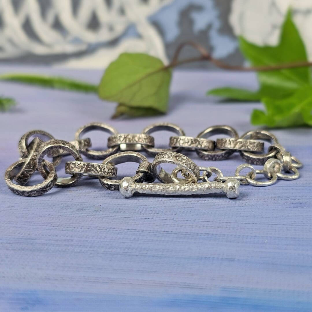 Chunky silver chain bracelet with hand etched leafy patterns and a forged toggle clasp, antique finish, lilac background, Isobel Kelly Jewellery