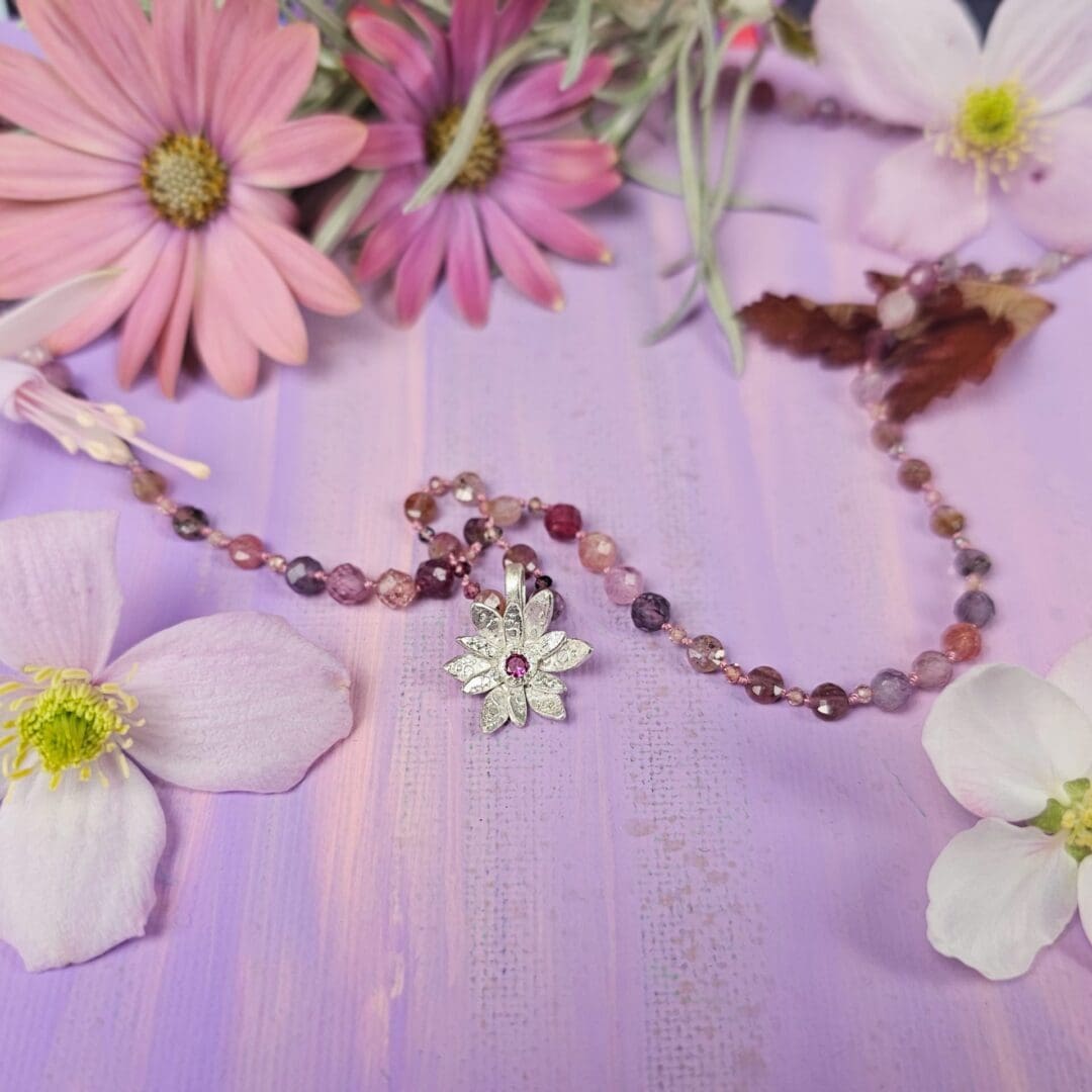 Spinel bead necklace with an etched silver flower pendant set with a small lab ruby at the centre, flower charm, pink background, Isobel Kelly Jewellery