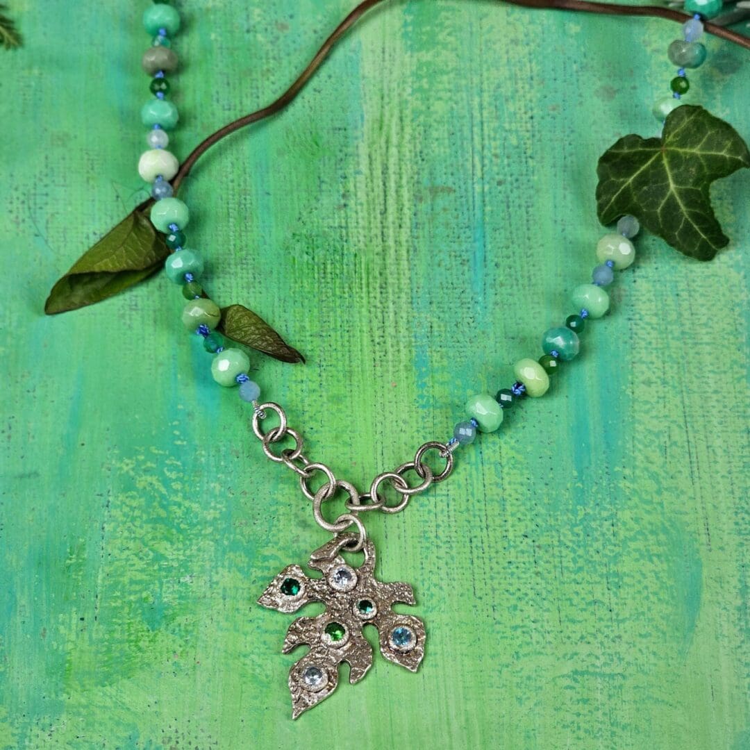 Silver leaf pendant set with lab emerald, topaz, tsavorite and spinel, pendant detail green background, Isobel Kelly Jewellery