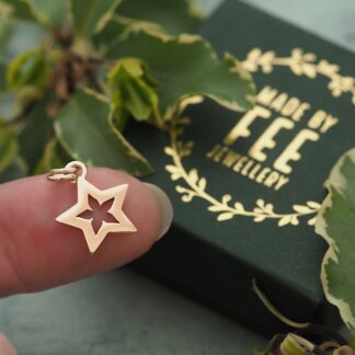 Handmade 9ct yellow gold open star flower pendant shown on finger for scale with Made By Fee presentation jewellery box