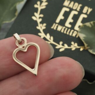 Handmade solid 9ct yellow gold open heart pendant shown on a finger for scale with a Made By Fee branded presentation jewellery box.