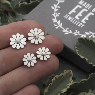 Two pairs of Argentium sterling silver daisy stud earrings handmade by Made By Fee. 10mm and 12mm diameter earrings shown on hand for scale