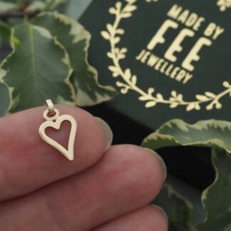 Dainty handmade solid 9ct yellow gold open heart pendant shown on a finger for scale with a Made By Fee branded presentation jewellery box.
