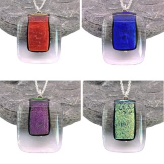 Four square glass pendants with silver chains, each featuring a colorful rectangular centerpiece in red, blue, purple, and green, displayed on stone.