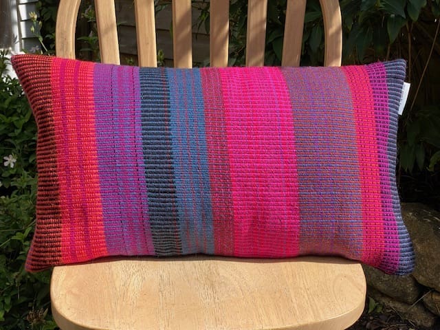 Large rectangular hand woven wool cushion ,featuring fuchsia pinks, warm reds and oranges.