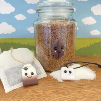Three kitchen canister tags - teabag, sugar cube and coffee bean. Each handmade from polymer clay. Shaped to represent each tag- teabag- a blend of white and brown with a tab on top with a small leaf. sugar cube- white glitter sparkling cube shape. Coffee Bean- chocolate brown, oval shape. Each one features a cute smiling face, black glass bead eyes, a big smile and rosy cheeks.