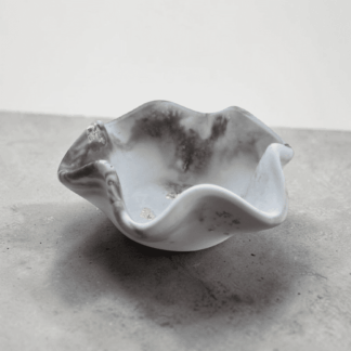 A small dish with wavy edges sits on a black and white marble counter in front of a plain white wall. The dish is black and white marble in colour.