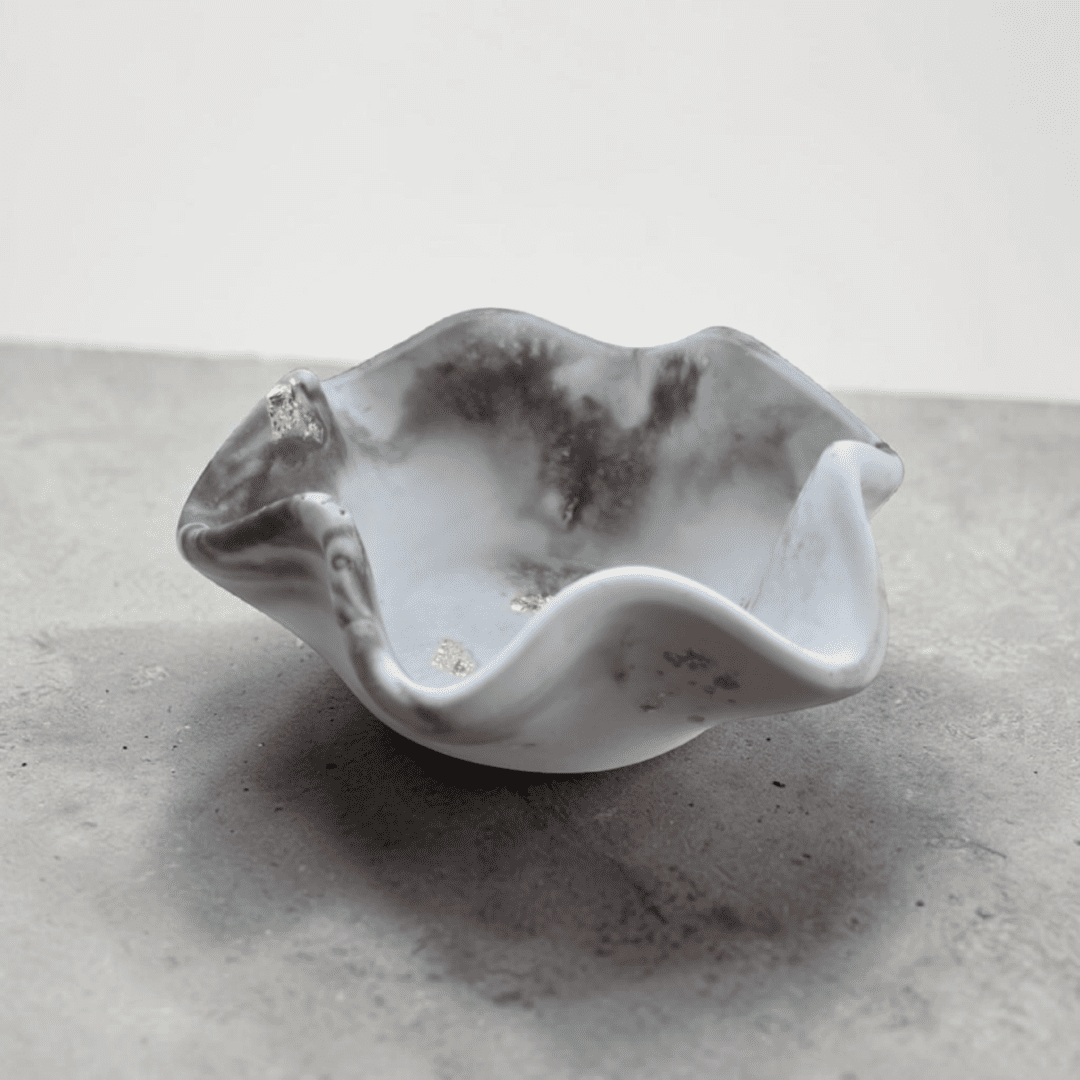 A small dish with wavy edges sits on a black and white marble counter in front of a plain white wall. The dish is black and white marble in colour.