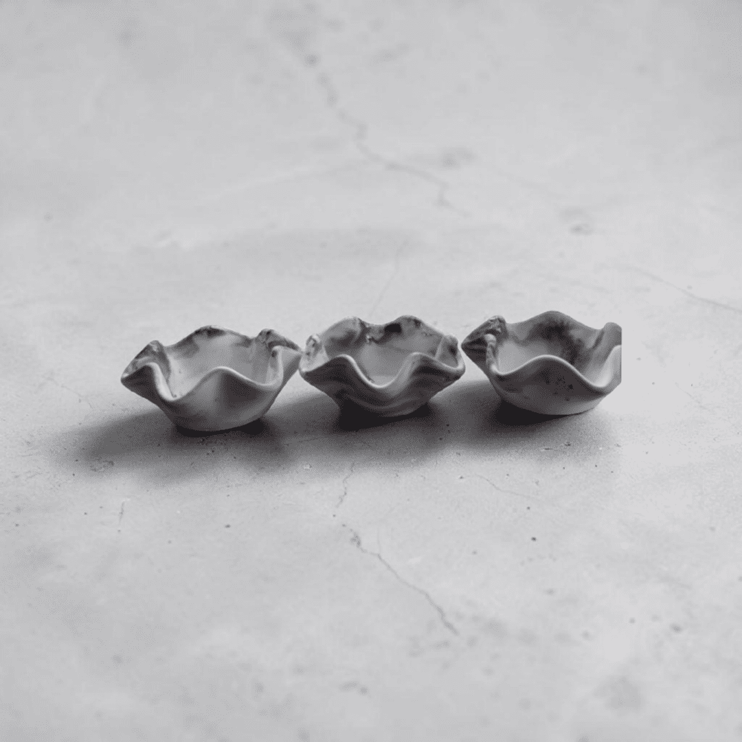Three small, wavy lipped dishes in black and white marble pattern sit in a row on a black and white marble counter.