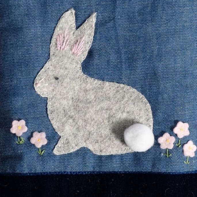 Close up of the rabbit on the glasses case showing the pompom tail, flowers and hand embroidered details for the ears, whiskers and eye