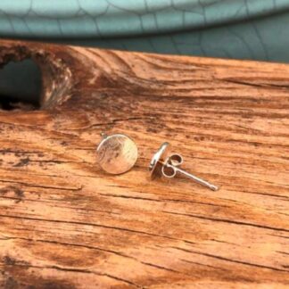 Handmade round recycled silver stud earrings with a subtle hammered finish, photographed on a piece of driftwood. Handmade in Cornwall.