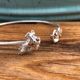 A handmade sterling silver bangle with organic water and salt cast details and tiny copper balls on each end. Sustainably made in Cornwall.