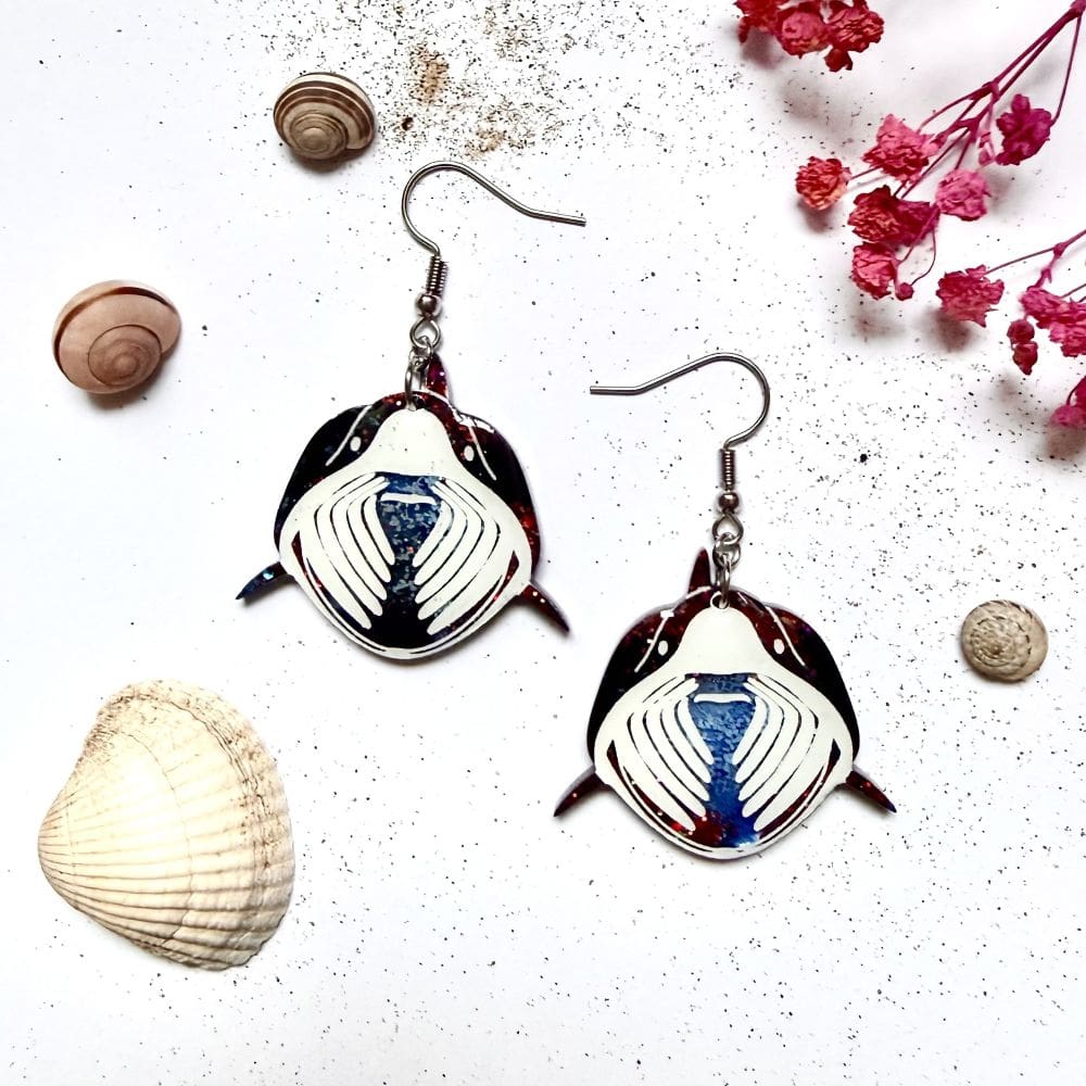Flat lay of zero waste black night basking shark resin earrings with ocean themed props, marine wildlife jewellery handmade UK Earrings are on hypoallergenic surgical steel ear hooks.