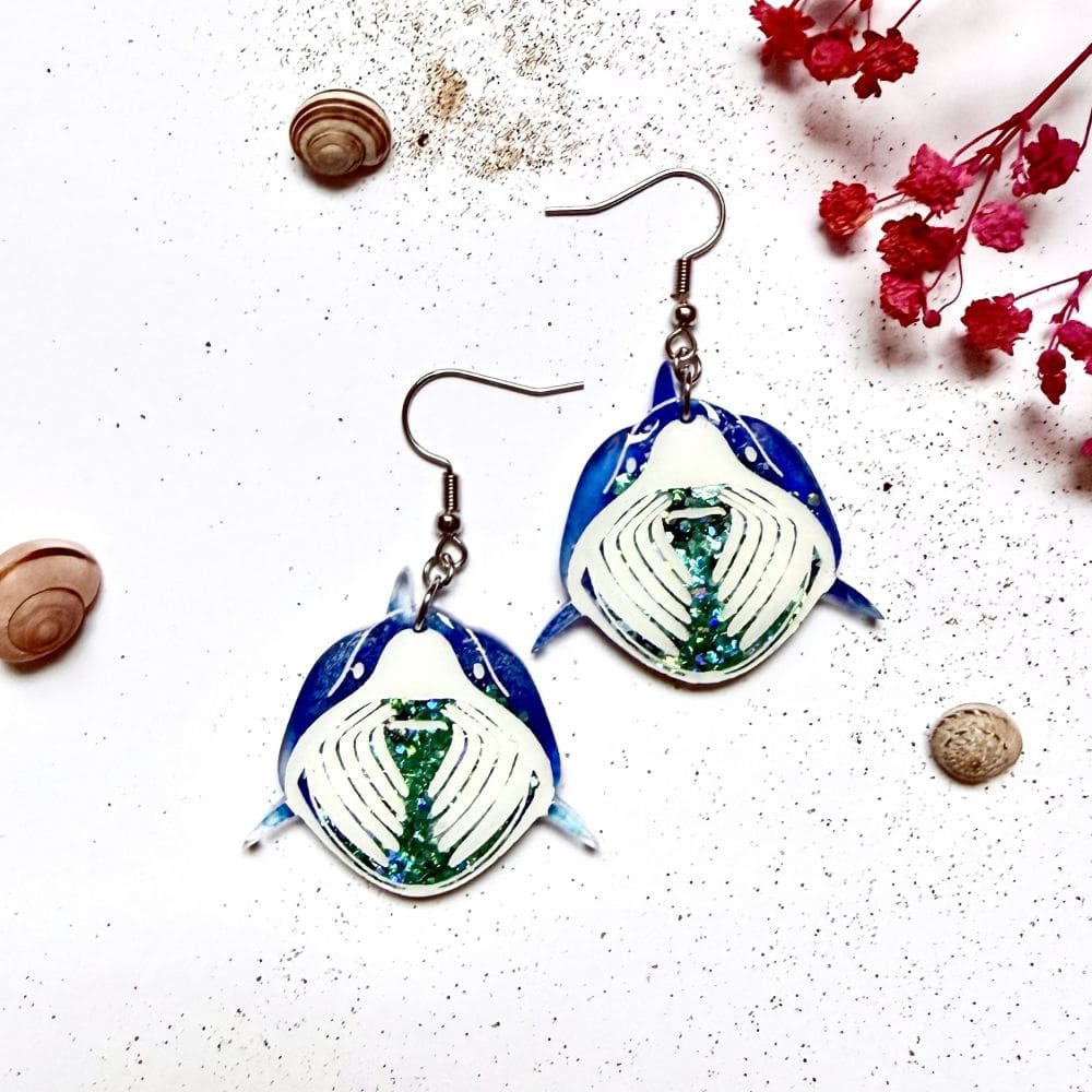 Flat lay of ocean blue mist basking shark resin earrings with ocean themed props, marine wildlife jewellery handmade UK. Earrings are on hypoallergenic surgical steel ear hooks.