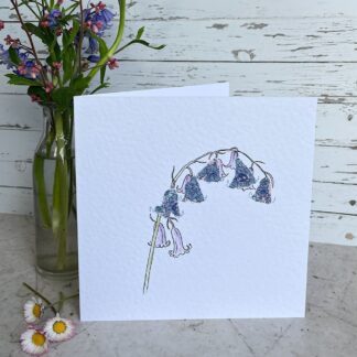 Greetings card with a single stem bluebell made with applique fabric. Stands next to a vase of dainty flowers