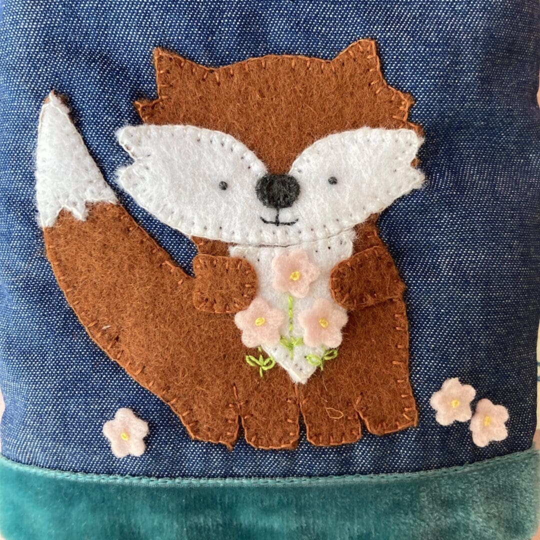 Close up of the felt fox I have hand sewn on to the denim showing the pink flowers and the leaves and stems I have hand embroidered