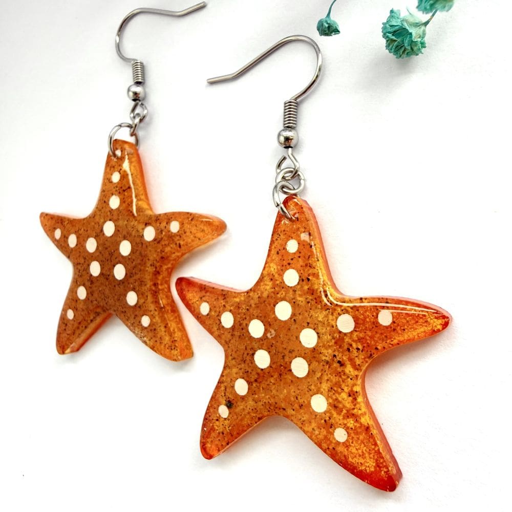 Flat lay of handmade starfish resin earrings. Unusual coastal ocean jewellery handmade Liverpool UK containing sand from Formby Beach near Liverpool, UK