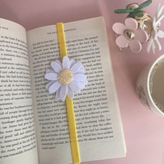 White felt daisy with a yellow centre, the centre is filled with sequins that shimmer in the light with a bright yellow velvet ribbon holding a page in a book