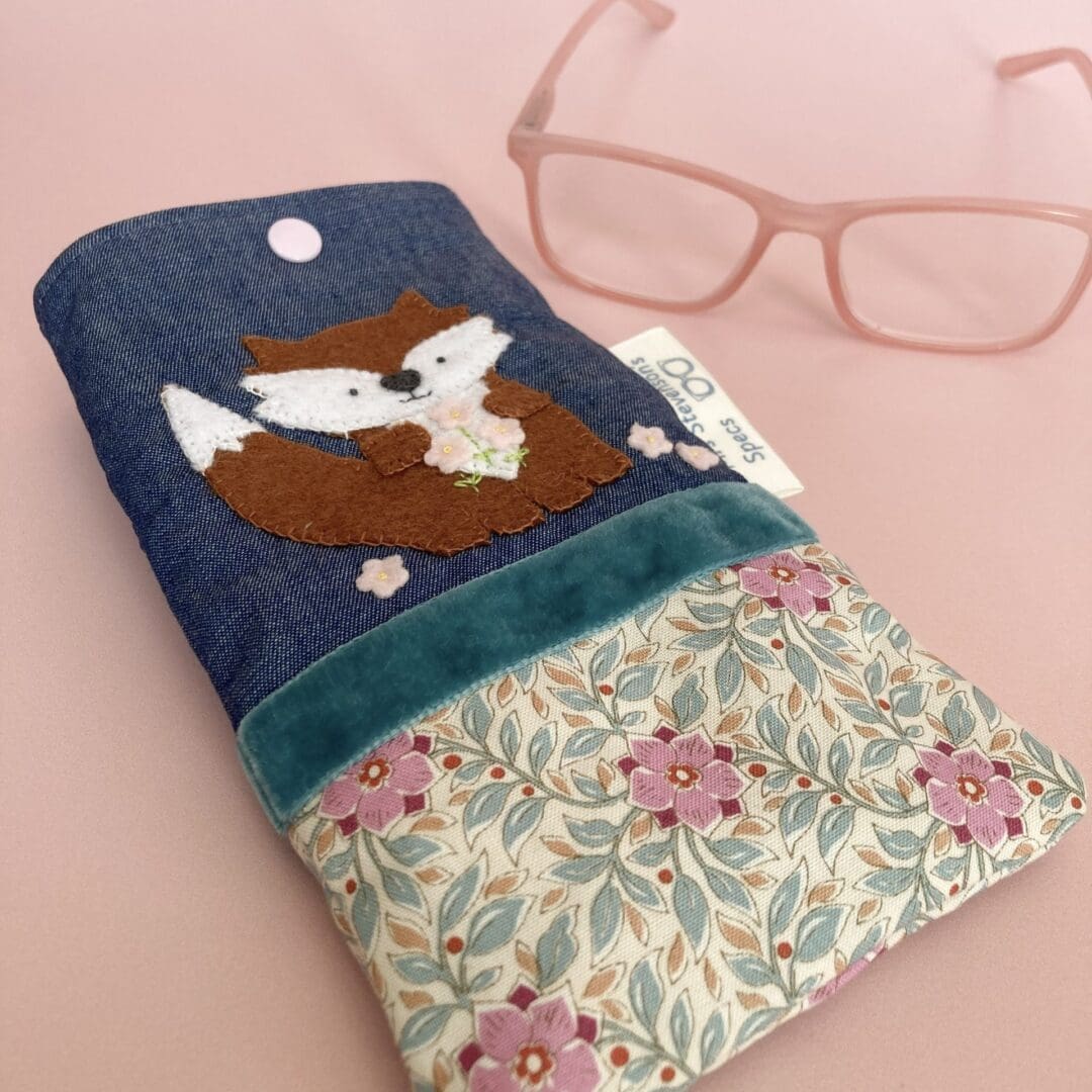 Glasses case at an angle beside a pair of pink reading glasses
