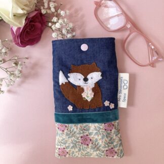 Handmade glasses case top section is denim which has felt fox sewn on it. The fox has a white face and tummy. The fox is holding 3 pretty pink felt flowers. The lower section is a pretty cream fabric with pink flowers. I had separated the denim and pretty fabric wit h a teal velvet ribbon. The glasses case closes with a pale pink snap fastener.