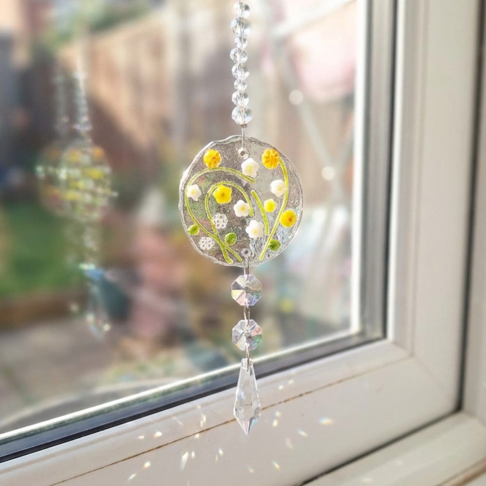 Fused glass floral disc suncatcher hanging against blurred garden background