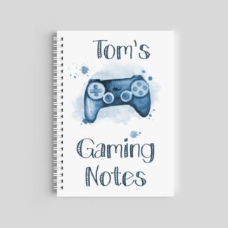 A spiral-bound notebook with a white cover featuring a blue watercolor game controller and blue paint splashes. The text reads "Tom's Gaming Notes" in a hand-drawn, outlined font.
