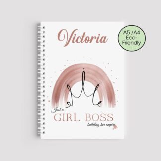 A spiral-bound notebook with a white cover. It features the name "Victoria" in rose gold, a watercolor rainbow with a black crown outline, and the text "Just a GIRL BOSS building her empire" at the bottom.