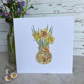 Greetings card featuring an floral fabric vase with fabric and hand drawn daffodils. Stands next to a vase of dainty flowers.