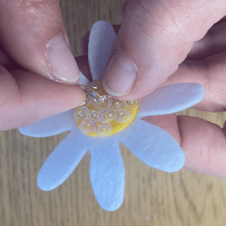Close up of me hand sewing sequins onto the centre of the daisy