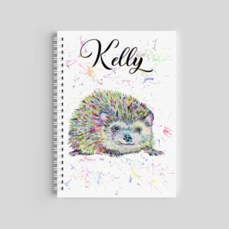 A spiral-bound notebook featuring a multi-colored watercolor hedgehog with a paint splash background. The name "Kelly" is printed at the top in an elegant black script font.