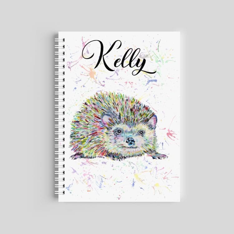 A spiral-bound notebook featuring a multi-colored watercolor hedgehog with a paint splash background. The name "Kelly" is printed at the top in an elegant black script font.