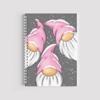 A spiral-bound A5 notebook with a grey background featuring three gnomes (gonks) with tall pink hats. White snow is falling all around them. The notebook has a white wire binding.