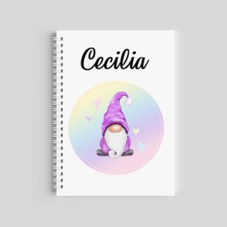 A spiral-bound notebook with a white cover. It features the name "Cecilia" at the top and a central illustration of a gnome with a purple hat inside a soft pastel rainbow circle with hearts.