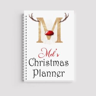 A spiral-bound notebook with a white cover featuring a large gold letter "M" with reindeer antlers and a red nose. Below, it reads "Mel's Christmas Planner" in red and black text.