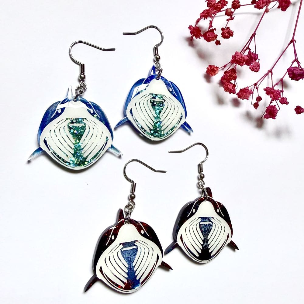 Side angle shot of two variations of Basking Shark earrings, ocean blue mist resin and sparkling green glitter detail on handmade basking shark and varation two black night glitter baskins shark earrings earrings UK
