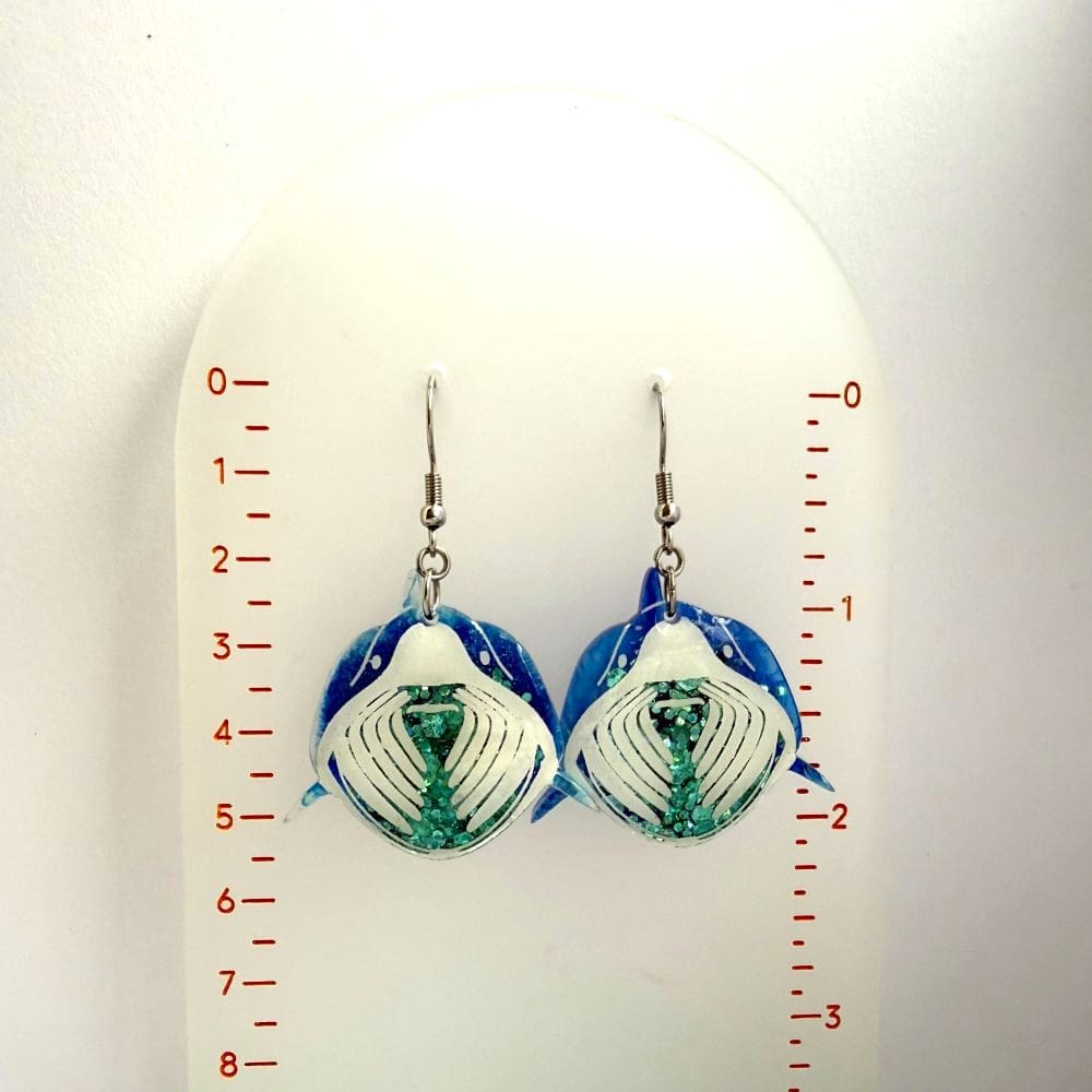 Scale size shot of handmade basking shark resin earrings by Copper Magpie Designs UK, displaged on a ruled hanger. Earrings are lightweight statement size and hypoallergenic.