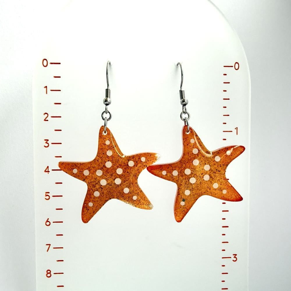 Scale size shot of handmade orange starfish resin earrings by Copper Magpie Designs Liverpool UK, surgical steel hooks