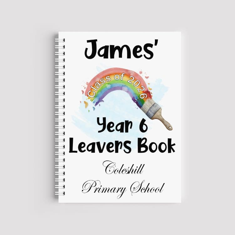 A spiral-bound A5 notebook with a white cover featuring a watercolor rainbow being painted by a brush. The text reads "James' Year 6 Leavers Book" and "Coleshill Primary School," with "Class of 2026" written across the rainbow arc.