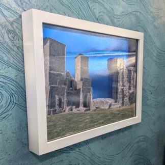 An A4 sized layered photo of Reculver Towers in Kent. Multiple cut layers stacked to make a 3D image on a blue mirrored background. Seen from the left edge and in a white box frame.