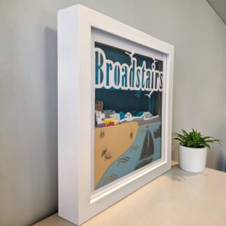 A 3D layered paper picture of Broadstairs Viking Bay in Kent. The background is blue mirror card and it ahs the word Broadstairs at the top of the front layer. It is in a white box frame and seen from the left edge.