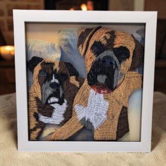 A quilled photo of 2 boxer dogs laying beside each other. The picture is in a square white 8" box frame