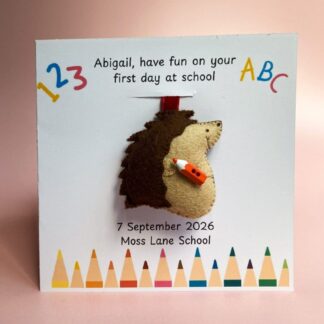 Personalised first day at school card with bright crayons at the bottom of the card, the card has a removable handmade hedgehog bag charm