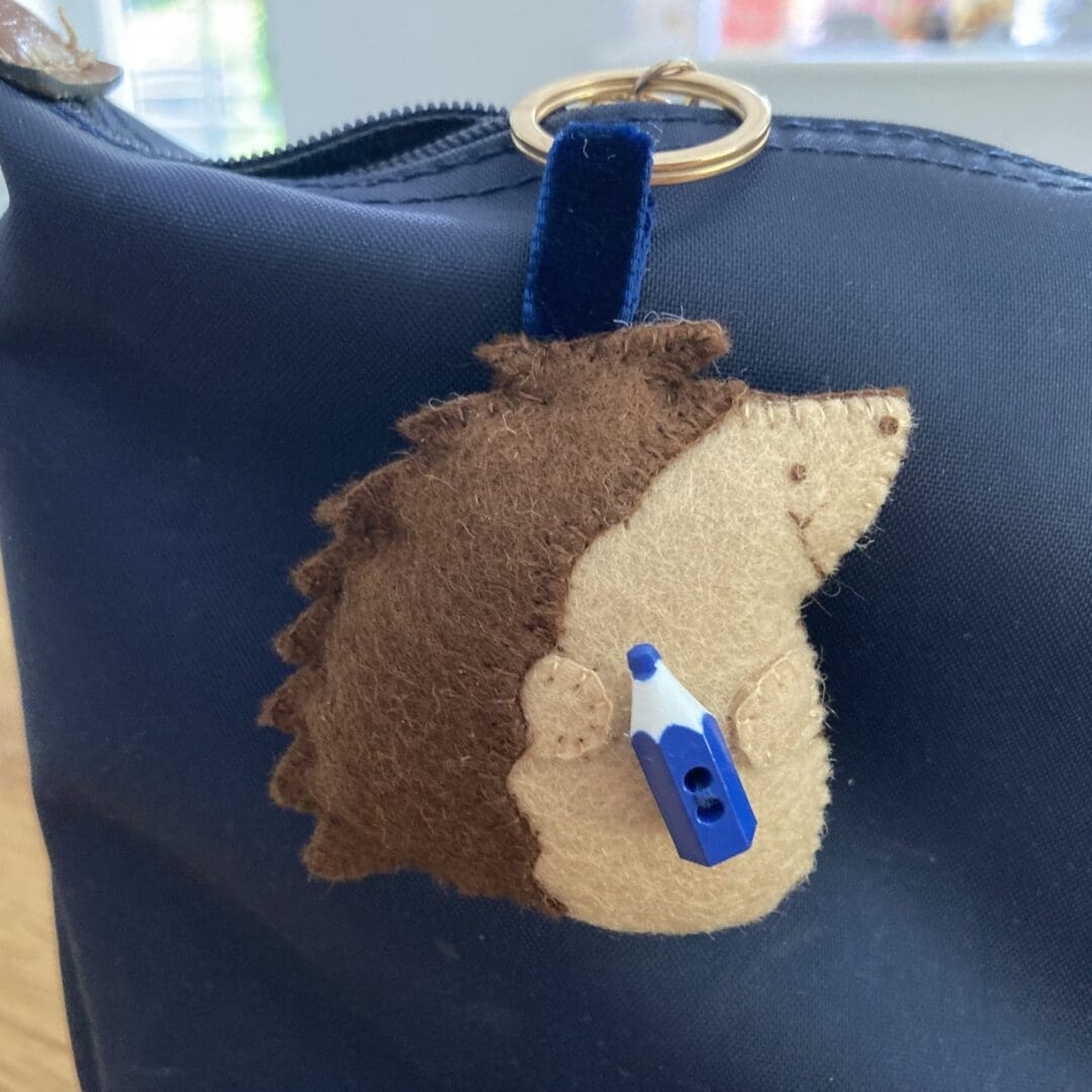Hedgehog bag charm with a blue pencil on a blue school bag