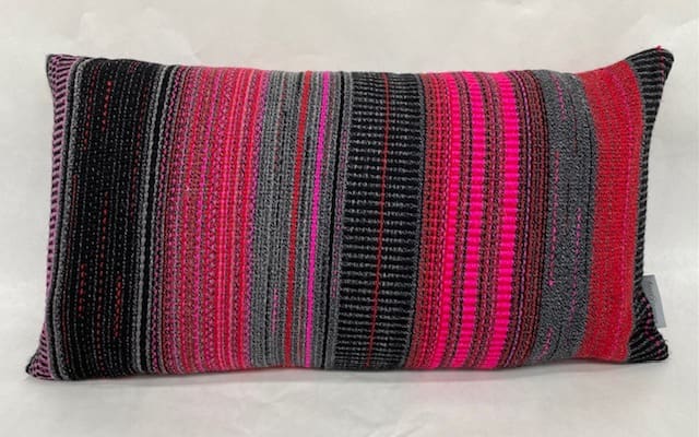 Contemporary hand woven wool cushion in a range of warm reds, soft greys and hot pinks.