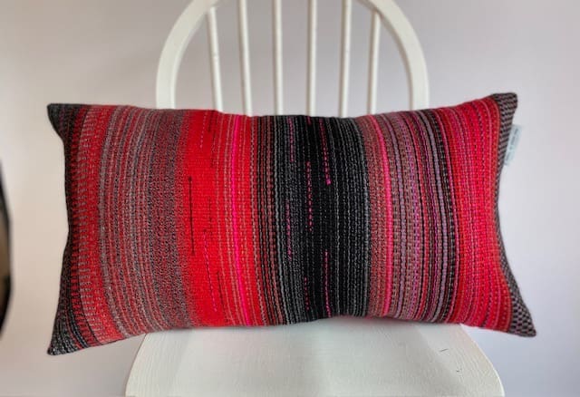 Contemporary hand woven wool cushion in a range of warm reds, soft greys and hot pinks. - Image 2