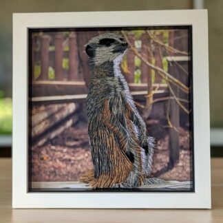 A quilled photo of a Meerkat sat up on a log protecting the colony. It is in a white box frame