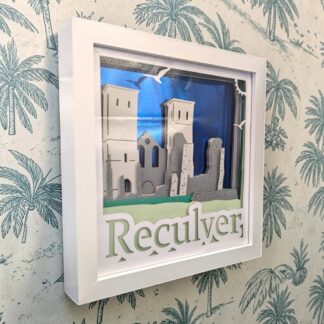 A layered artwork of Reculver Towers in Kent with a blue mirrored background and the remains of the Roman fort with the refurbished remaining towers. Seen from the left edge and in a white box frame