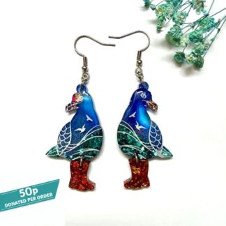 Pair of handmade seagull resin earrings with red glitter boots and real Formby Beach sand by Copper Magpie Designs Liverpool. Displayed on a white background with blue flowers. 50p from each order is donated to marine charities.