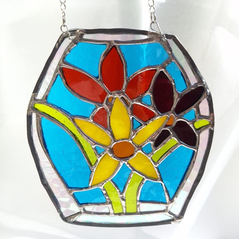 Handmade stained glass daffodil suncatcher with yellow and red flowers on a turquoise blue background