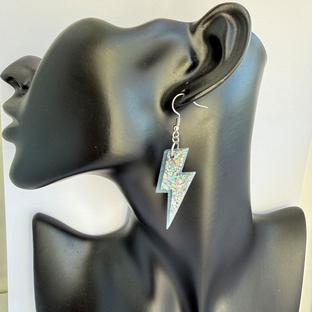 Worn image of a model wearing handmade holographic lightning bolt resin earrings, festival statement jewellery by Copper Magpie Designs.